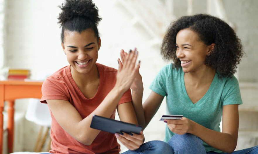 mmm/Two cheerful mixed race curly girlfriends shopping online with tablet computer and credit card at home